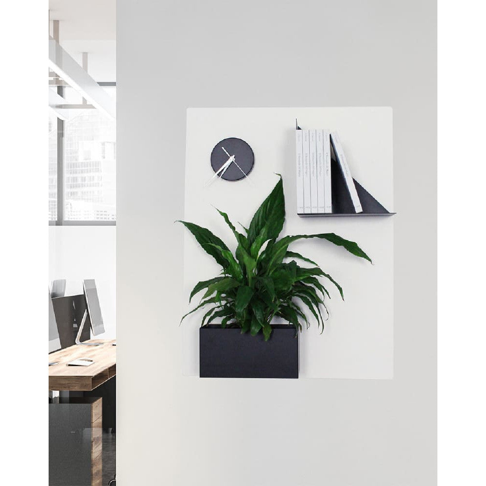 In einem klar strukturierten Office hängt die weiße Kreidetafel mit magnetischem Bücherregal, Pflanzgefäß und Uhr – schafft Ruhe, Übersicht