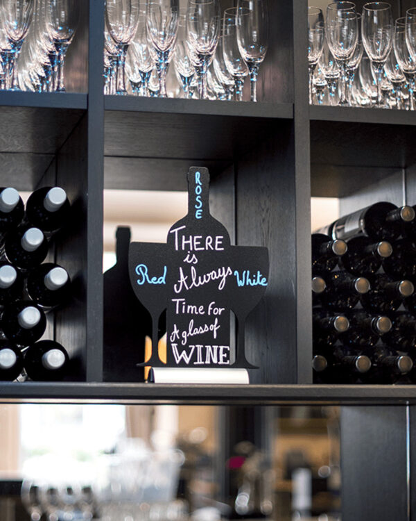 Tischkreidetafel in Weinflaschen Form Silhouette beschriftet mit einem Weinspruch und aufgestellt in einer Vinothek im Weinregal